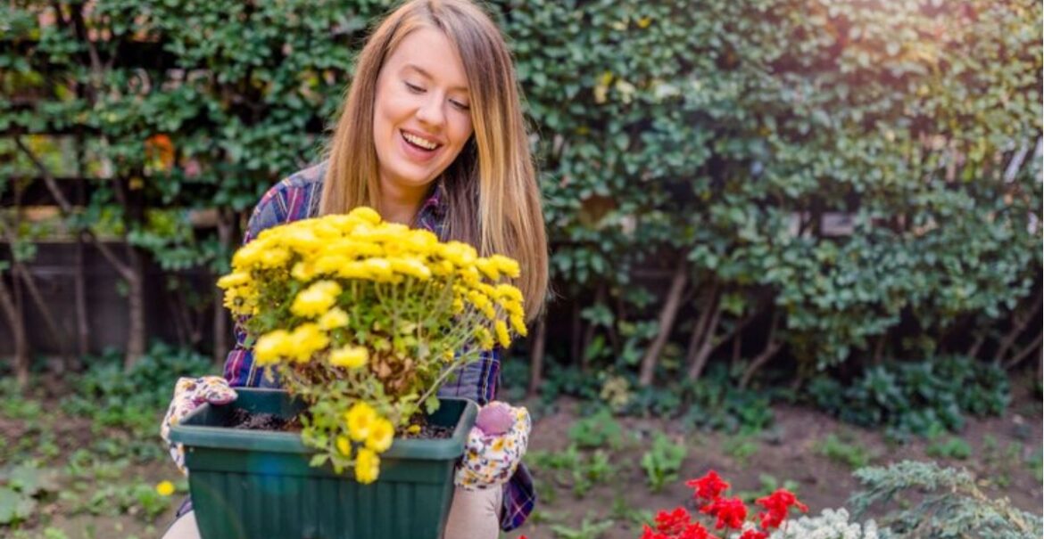 young-smiling-woman-florist-working-garden-portrait-smiling-young-woman-holding-pot-with-beautiful-flowers-garden