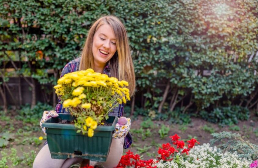 young-smiling-woman-florist-working-garden-portrait-smiling-young-woman-holding-pot-with-beautiful-flowers-garden